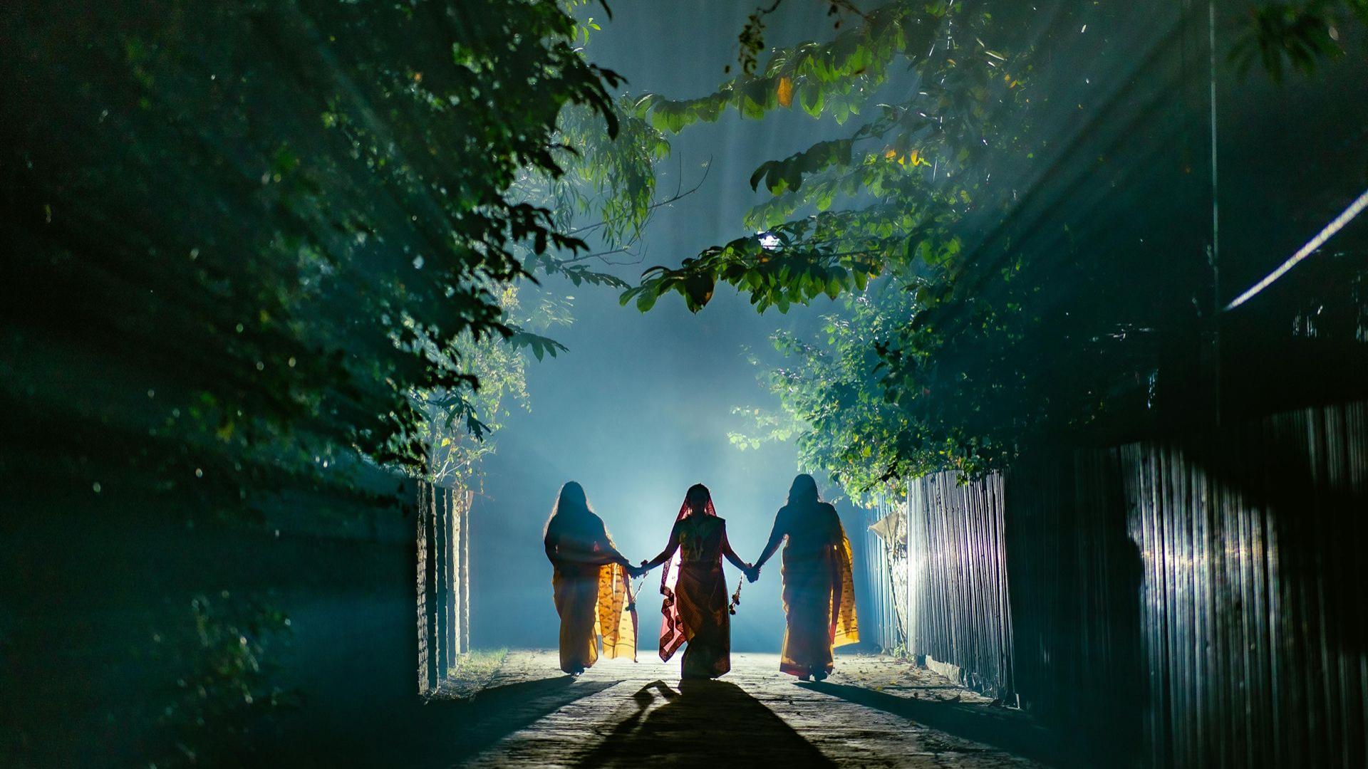 Drei Gestalten, die nachts Hand in Hand auf einem nebligen Waldweg spazieren.